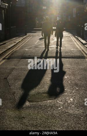 Fußgänger, die durch das Licht am späten Nachmittag beleuchtet werden, laufen entlang der Fashion Street, Spitalfields, London, Großbritannien. April 2023 Stockfoto