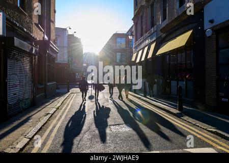 Fußgänger, die durch das Licht am späten Nachmittag beleuchtet werden, laufen entlang der Fashion Street, Spitalfields, London, Großbritannien. April 2023 Stockfoto