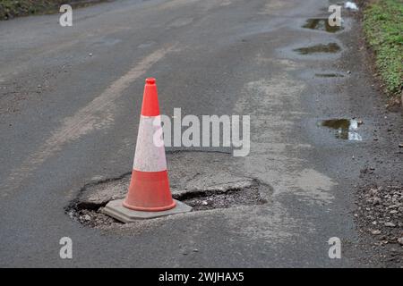 Buckinghamshire, Großbritannien. Februar 2024. Ein Verkehrskegel in einem Schlagloch warnt Autofahrer in Potter Row, Buckinghamshire. Die Anzahl der Schlaglöcher, die auf den Straßen in Buckinghamshire auftauchen, bereitet weiterhin Probleme. Die jüngsten starken Regenfälle haben das Problem noch verschärft. Der Buckinghamshire Council hat angeblich 28 Teams, die diesen Monat Schlaglochreparaturen durchführen. Obwohl HS2 eine Reihe von Transportstraßen gebaut hat, um ihre LKW zu nehmen, gibt es immer noch HS2-LKW, die Straßen in ganz Buckinghamshire nutzen, was das Schlaglochlück noch verschärft. Kredit: Maureen McLean/Alamy Stockfoto