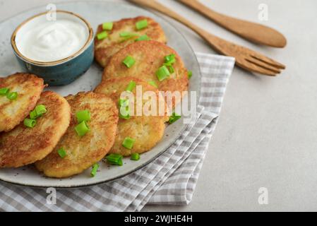 Kartoffelpfannkuchen oder Latkes oder Draniki mit Sauerrahm in Teller auf hellem Hintergrund. Kopierbereich. Stockfoto