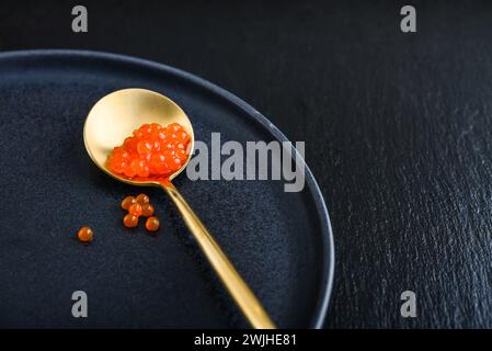 Roter Kaviar im goldenen Löffel auf schwarzem Schieferhintergrund Closeu Stockfoto