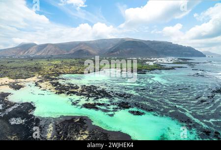 Entdecken Sie das ruhige Caletón Blanco auf Lanzarote, wo vulkanische Felsen türkisfarbenes Wasser vor dem Hintergrund dramatischer Berge umgeben. Stockfoto