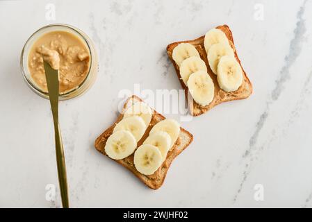 Erdnussbutter-Sandwich mit frischen Bananenscheiben auf Marmortisch, Blick von oben Stockfoto