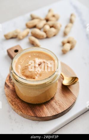 Cremige und glatte Erdnussbutter im Glas Erdnüsse in Schale auf Marmortisch. Natürliche Ernährung und Bio-Lebensmittel. Stockfoto