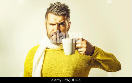 Kaffeepause. Schöner Mann mit Bart und Schnurrbart in gelbem Pullover und weißem Schal mit einer Tasse Kaffee. Stilvoller bärtiger Mann mit einer Tasse Tee Stockfoto