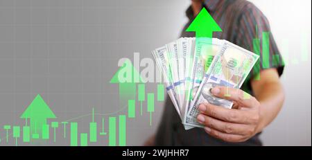 Wirtschaftswachstumskonzept. Bargeld in der Hand eines Mannes mit Aufwärtspfeil und steigendem Diagramm. Der Dollar wächst stark und erhöht seine Aufwertung und sein Geldangebot. Stockfoto