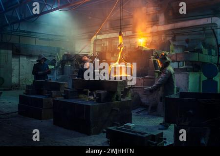 Arbeiter gießen geschmolzenes Metall in der Stahlgießerei. Industrieteam im Bereich des Schutzgetriebes, Herstellung in der Schwerindustrie. Heißmetallschmieden, Teamwork Stockfoto