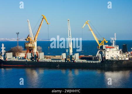 Frachtschiff, das Container im belebten Seehafen lädt. Industriekrane heben Güter für den internationalen Transport auf ein Schiff. Globaler Handel, Logistik Stockfoto