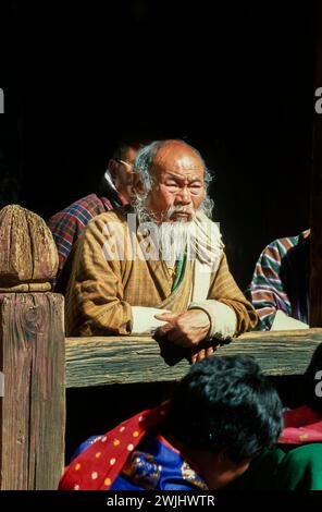 Lokale Zuschauer beim Jakar Dzong Tsechu, einem beliebten jährlichen religiösen und kulturellen Festival, das im Oktober in Jakar Dzong im Bumthang-Tal im Zentrum von Bhutan gefeiert wird. Eine Vielzahl von bunten Maskentänzen werden von Mönchen durchgeführt, die nach präzisen Anweisungen früherer buddhistischer Meister entwickelt werden. Ein älterer Mann aus der Gegend mit einem bärtigen Bart sieht sich die Vorstellung an. Stockfoto