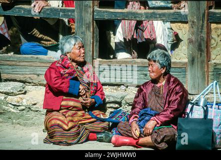 Zwei Seniorinnen in typisch lokaler Kleidung plaudern miteinander, Zuschauer beim Jakar Dzong Tsechu, einem beliebten jährlichen religiösen und kulturellen Festival, das im Oktober in Jakar Dzong im Bumthang-Tal im Zentrum von Bhutan gefeiert wird. Eine Vielzahl von bunten Maskentänzen werden von Mönchen durchgeführt, die nach präzisen Anweisungen früherer buddhistischer Meister entwickelt werden. Aufgenommen im Jahr 2001. Stockfoto