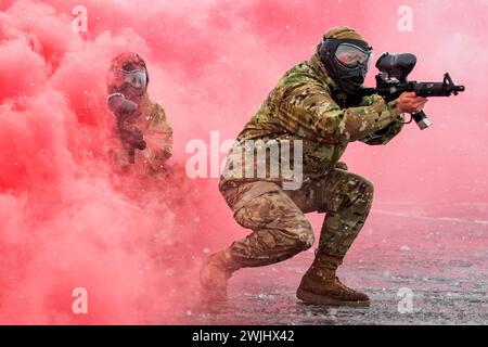 Boise, Idaho, USA. Februar 2024. Ein US-Luftmann von der Idaho Air National Guards 124th Medical Group hält seine Waffe fest vor sich, drückt sie gegen seine Schulter, Finger am Abzug, seinen Körper tief zum Boden. Er macht einen kleinen, strategischen Schritt in die Rauchwolke, die um ihn herum wirbelt. Umgeben von einer Decke aus rotem Rauch ist es schwer, seinen Kampfkumpel zu sehen, aber er weiß, dass sein Gegenstück, ein Soldat der Idaho Army National Guards Charlie Company, 145th Brigade Support Battalion Medical Detachment, nahe hinter ihm ist. Etwa 200 Idaho National Guar Stockfoto