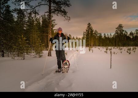 Frauen mittleren Alters in Schneeschuhen, die am Waldrand posieren und einen Schneeschuh hochgehoben haben. Nahaufnahme des Fotos Stockfoto