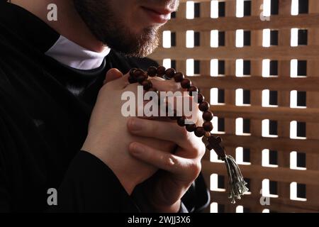 Junger Priester betet in Beichtkabine, Nahaufnahme Stockfoto