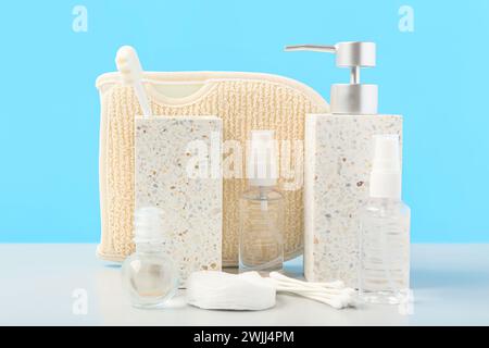 Komposition mit Wattestäbchen, Duschgel und Flaschen kosmetischer Produkte auf dem Tisch in der Nähe der blauen Wand. Badezimmerzubehör Stockfoto