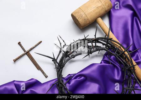 Dornenkrone mit violettem Stoff, Hammer und Nägeln auf weißem Hintergrund Stockfoto