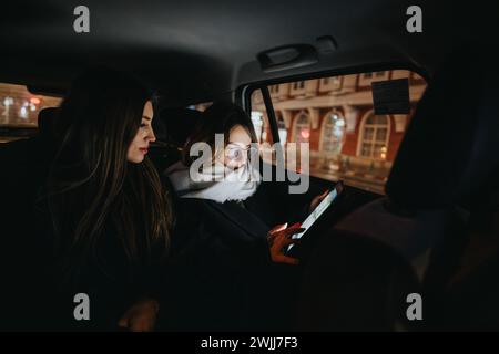 Junge Frauen, die ihr Smartphone zusammen auf dem Rücksitz des Autos benutzen. Stockfoto