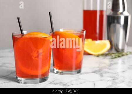 Aperol Spritz Cocktail, Orangenscheiben und Strohhalme in Gläsern auf weißem Marmortisch Stockfoto