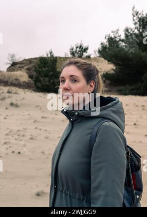 Porträt einer nachdenklichen jungen Frau in den Sanddünen. Blondes Haar wurde ordentlich zurückgezogen, während sie mit nachdenklichem Ausdruck in die Ferne blickt Stockfoto