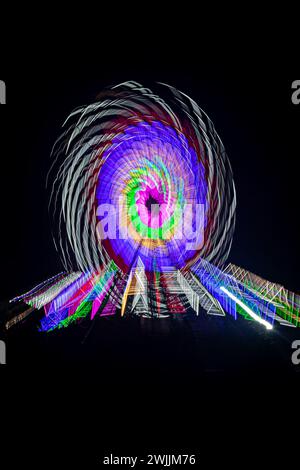 Absichtliche Kamerabewegung, Slow Shutter Zoom Unschärfe das Bild eines Riesenrads, das nachts auf einem Jahrmarkt beleuchtet und dreht. Stockfoto