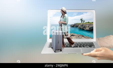 Eine menschliche Hand, die einen Laptop hält, mit einem asiatischen Mädchen in einem Hut und einem Koffer mit einer Klippe und Meerblick auf dem Laptop-Bildschirm. Reisekonzept Stockfoto