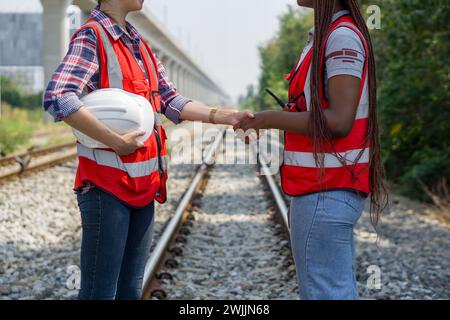 Zwei Frauen mit Schutzhüten schütteln auf einigen Bahngleisen die Hand. Stockfoto