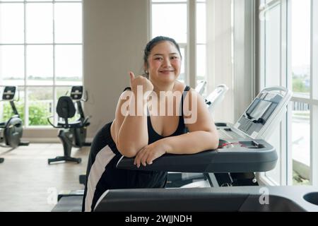 Eine Frau in Übergröße steht auf einem Laufband im Fitnessstudio, ruht sich aus oder bereitet sich auf das Training vor. Stockfoto