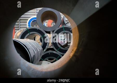 Stapel von silbernen Stahlspulen werden in einer großen, geschäftigen Fabrikumgebung gestapelt. Stockfoto