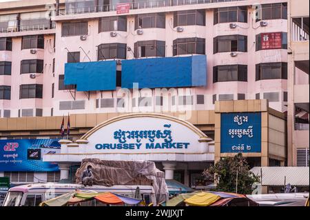 Das zweisprachige Schild am Eingang zum Orussey Market. Ein kambodschanischer Mann hockt, während er eine Schutzmaske trägt. Phnom Penh, Kambodscha. © Kraig Lieb Stockfoto