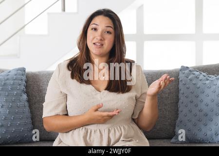 Eine junge birassische Frau sitzt bei einem Videoanruf bequem zu Hause auf einer Couch Stockfoto