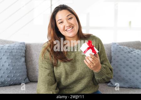 Junge Frau mit einer Geschenkbox zu Hause bei einem Videoanruf, mit Kopierraum Stockfoto