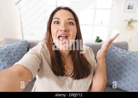 Eine junge birassische Frau macht ein verspieltes Selfie zu Hause bei einem Videoanruf Stockfoto