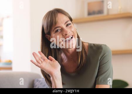 Eine weiße Frau mittleren Alters lächelt, winkt der Kamera bei einem Videoanruf zu Stockfoto