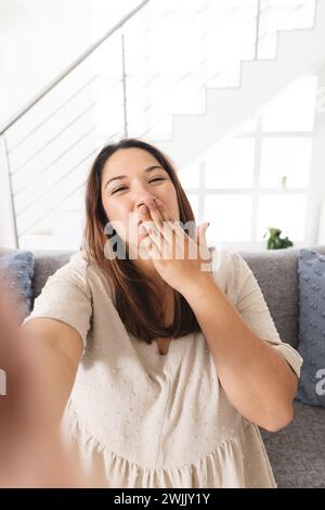 Eine junge birassische Frau macht zu Hause ein Selfie bei einem Videoanruf und bläst einen Kuss Stockfoto