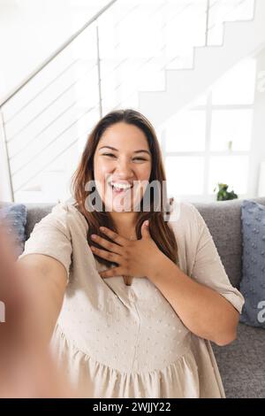 Fröhliche, junge Frau in Übergröße, die zu Hause ein Selfie macht, mit Kopierraum Stockfoto