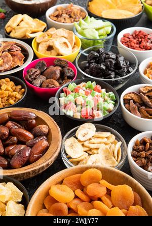 Mischung aus gesunden getrockneten süßen Früchten und Beeren in verschiedenen Schälchen auf schwarzem Hintergrund. Stockfoto