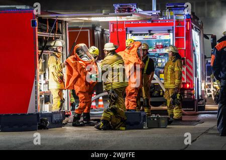 Esslingen, Deutschland. Februar 2024. Feuerwehrleute in Schutzanzügen bereiten sich auf ihre Reaktion auf einen Gefahrgutunfall vor. Bei Ladearbeiten auf einem Werksgelände in Esslingen am Neckar wurde ein Container mit Gefahrgütern durch einen Gabelstapler beschädigt. Mehrere hundert Liter Chlorwasserstoff sind Freitagnacht aus dem Behälter ausgetreten, was laut der Feuerwehr eine spürbare Rauchmenge verursacht hat. Quelle: Kohls/SDMG/dpa/Alamy Live News Stockfoto