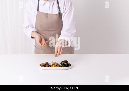 Die Frau streut Sesamsamen mit den Händen auf das fertige Gemüsegericht Stockfoto