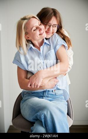 Niedlicher Familienmoment, in dem Mom und Tochter umarmen. Nahporträt eines Teenagers, das Mutter ihre Liebe zeigt. Zwei Frauen in lässiger Kleidung, die sich zu Hause mit geschlossenen Augen umarmen. Stockfoto