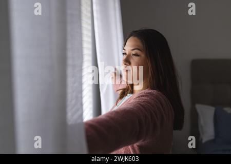 Eine junge Frau in Übergröße schaut nachdenklich zu Hause aus dem Fenster Stockfoto