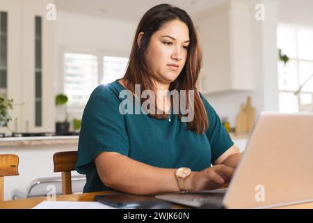 Eine junge Frau in Übergröße arbeitet fleißig an ihrem Laptop zu Hause, unverfälscht Stockfoto