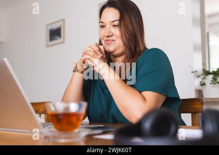 Eine junge Frau in Übergröße lächelt, während sie zu Hause an ihrem Laptop arbeitet Stockfoto