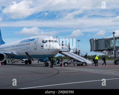 Kaliningrad, Russland - 12. Oktober 2023: Reisende, die die Luftreppen hinaufsteigen, um an Bord eines kommerziellen Flugzeugs auf der Asphaltbahn unter klarem blauem Himmel zu gehen. Stockfoto