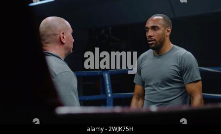 Ein professioneller Trainer spricht und bringt afroamerikanischen Boxern den Kampf am Boxring bei. Sportlicher Mann hört Trainer, Übungen, bevor er die Meisterschaft kämpft. Körperliche Aktivität und intensives Training. Stockfoto