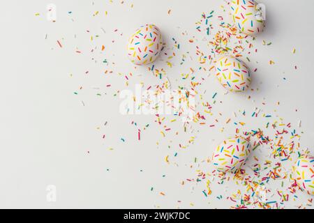 Farbenfrohe ostereier auf weißem Hintergrund mit ausgelaufenen Kuchenstreuseln. Direkt über der Tischplatte. Stockfoto