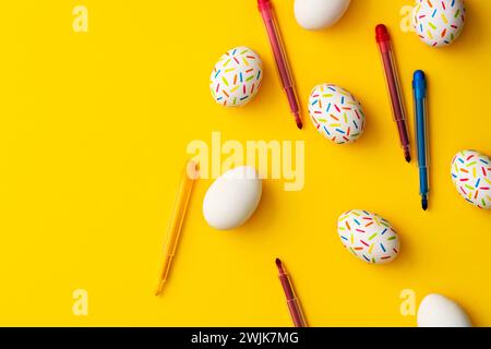 Bestreuen Sie farbige ostereier mit Farbstiften auf gelbem Hintergrund. Direkt über der Tischplatte. Stockfoto