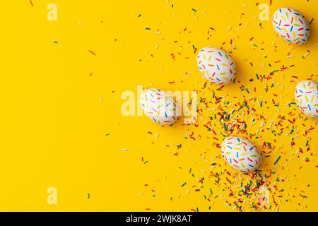 Bestreuen Sie farbige ostereier auf gelbem Hintergrund. Direkt über der Tischplatte. Stockfoto