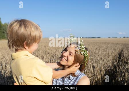 Glückliche Mutter und Sohn auf einem Weizenfeld, der Junge hält sanft den Kopf seiner Mutter. Das Konzept der elterlichen Liebe, Mutterschaft. Muttertag. Genießen Sie die Natur und das Leben Stockfoto