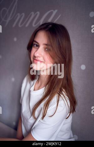 Das schöne Teenager-Mädchen sitzt auf einem Bett in der Nähe der Wand mit ihrem Namen drauf Stockfoto