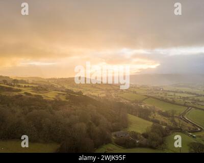 Sonnenaufgang über sanften Hügeln und Ackerland in Denbighshire, mit frühmorgendlichem Licht, das durch Wolken über der ländlichen walisischen Landschaft bricht. Stockfoto