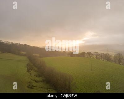 Sonnenaufgang über sanften Hügeln und Ackerland in Denbighshire, mit frühmorgendlichem Licht, das durch Wolken über der ländlichen walisischen Landschaft bricht. Stockfoto